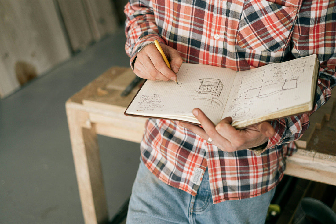 A man wearing holding a notebook and sketching ideas