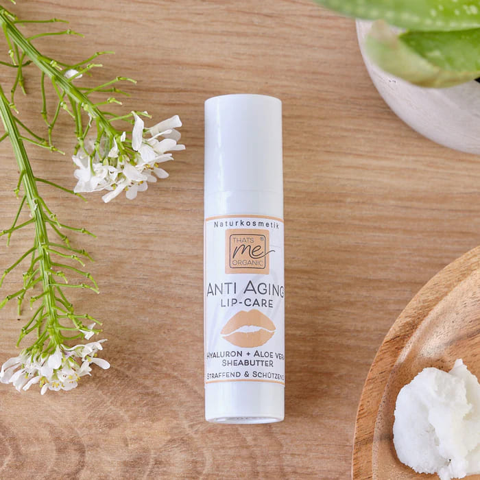 Organic lip balm placed on a wooden table with white flowers and a shea butter scoop.