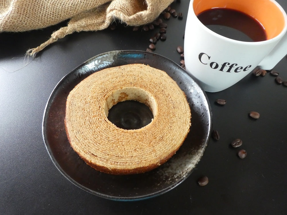 Baumkuchen with Hawaiian coffee flavor on a dark plate, served with hot coffee. soft, moist, and crafted with care.