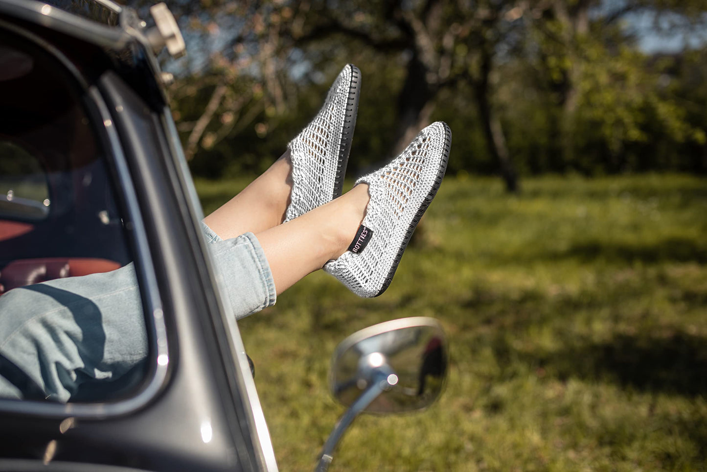 Legs wearing peppermint crocheted Botties sticking out of a car window, with a green field in the background