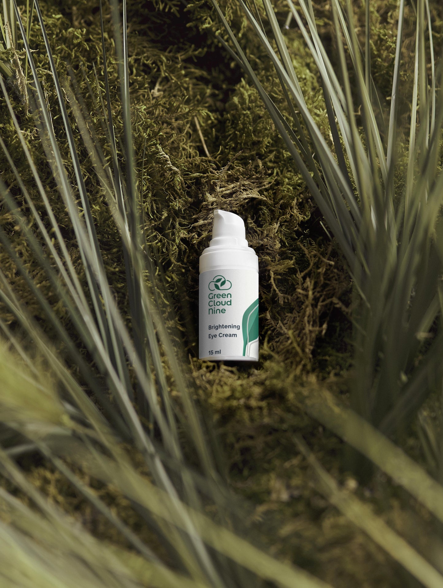Brightening Eye Cream White bottle pump with Green Cloud Nine label on a bed of green plants (front).