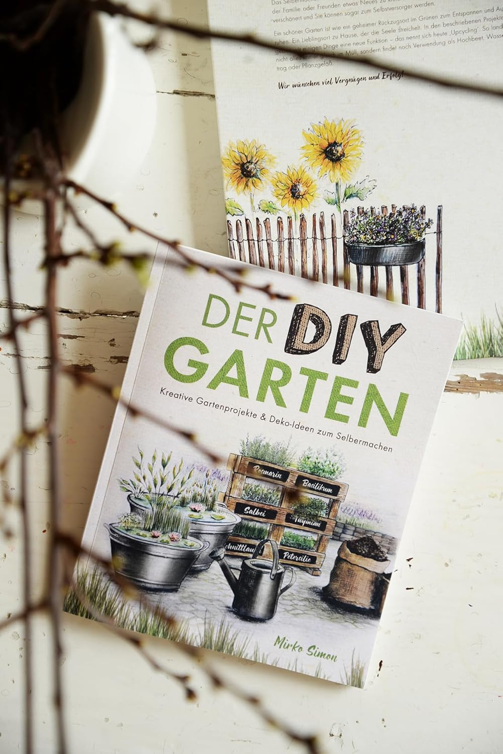 Book titled 'Der DIY Garten' on a wooden surface with plants and gardening elements.