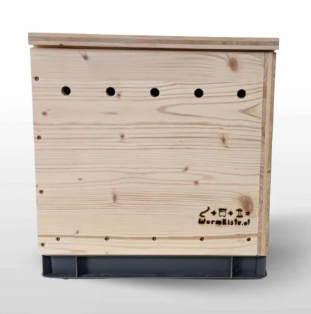 Closed wooden worm composting box with ventilation holes and a plastic base, placed against a white background