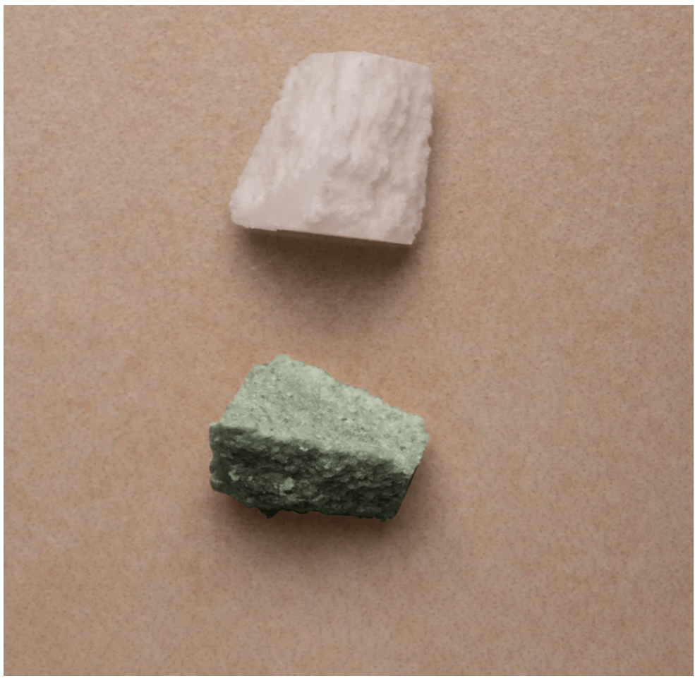 Close-up of broken pieces of Rosental solid shampoo and conditioner bars in green and beige on neutral background.