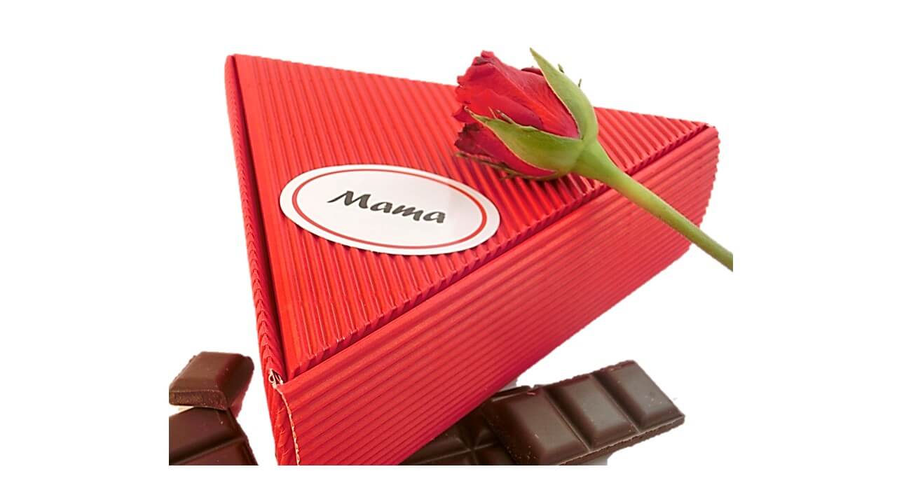 Photo of a red triangular gift box labeled “Mama,” topped with a red rose and surrounded by pieces of chocolate