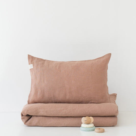 A neatly folded natural linen blanket in a cafe creme tone with a matching pillow placed on top from Duvet Cover Set for Kids