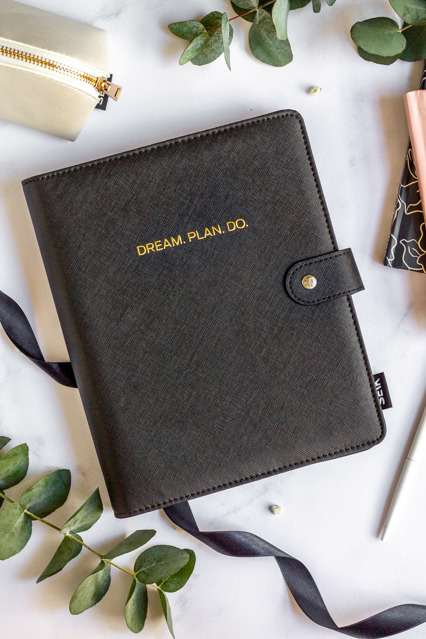 Eco-friendly Refillable Notebook with vegan leather, placed on a white table with green leaves, a pen, and a pouch.