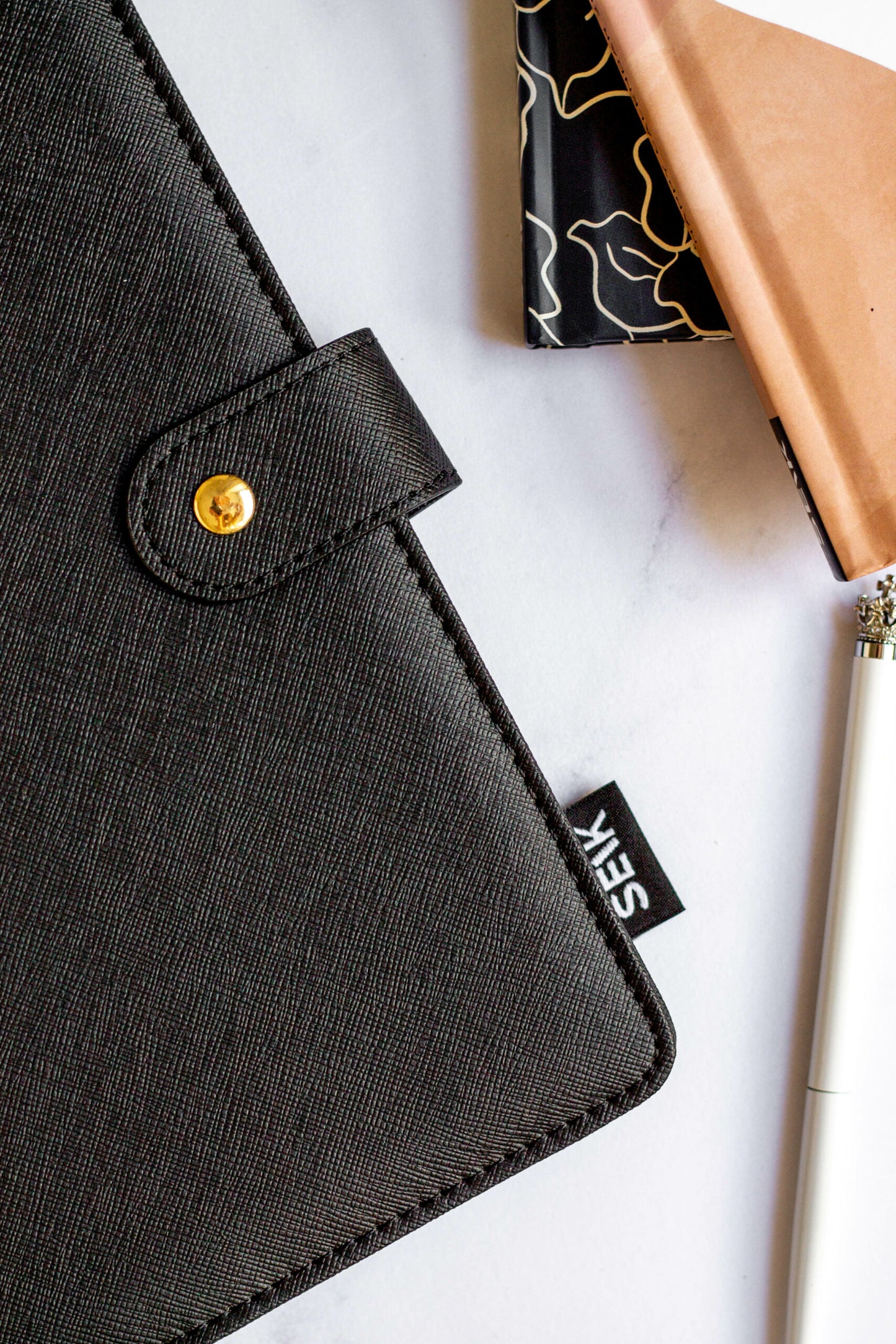 Detail of Eco-friendly Refillable Notebook with vegan leather, placed on a white table with green leaves, a pen, and a pouch.