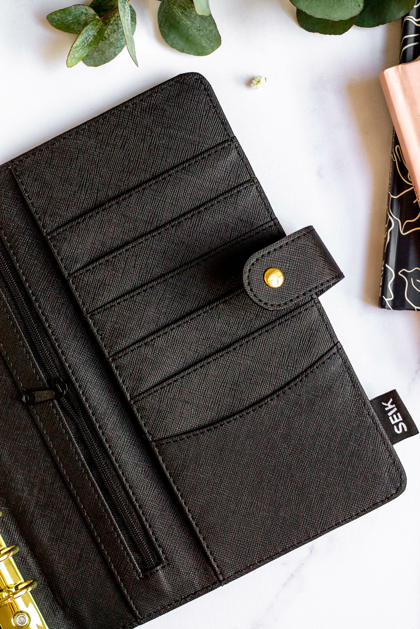Interior detail of Eco-friendly Refillable Notebook with vegan leather, placed on a white table with green leaves, a pen, and a pouch.