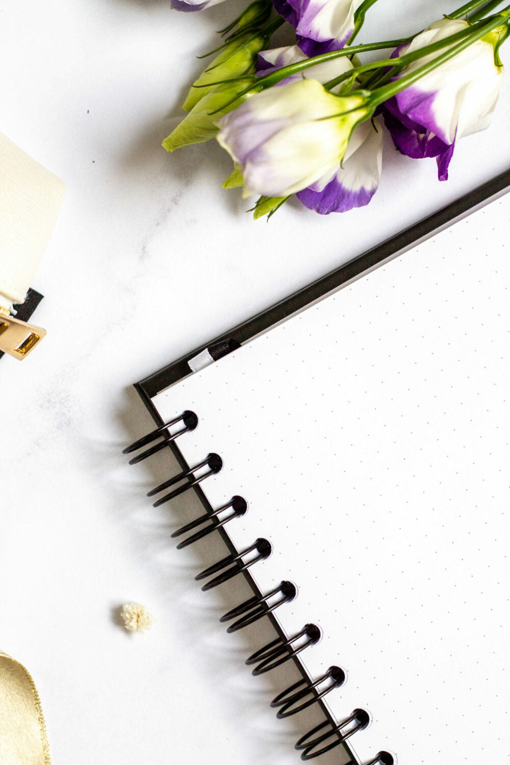 Close-up of an open spiral-bound Eco-friendly Refillable Notebook. Purple and white flowers are placed at the top