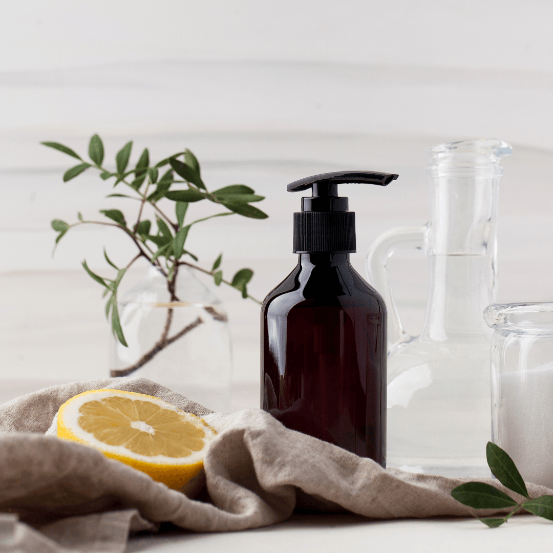 Amber bottle with pump surrounded by lemon, leaves, and glassware on linen