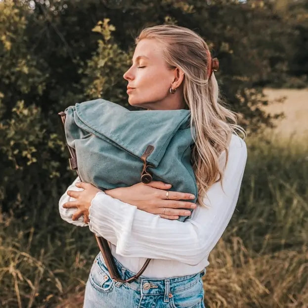 Woman outdoors holding a turquoise canvas handbag with leather strap, wearing jeans and white top.