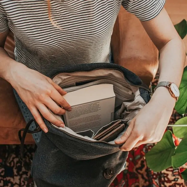 Woman opening Turquoise canvas handbag filled with books and a wallet, seated indoors on a patterned carpet.