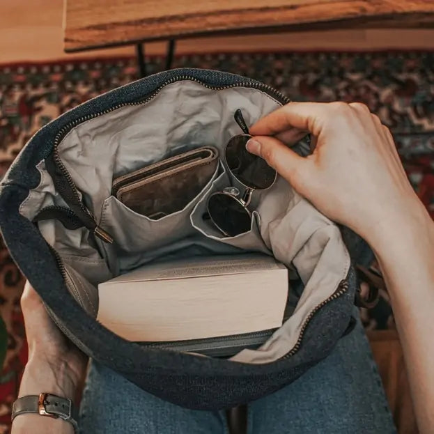 Open  Turquoise canvas handbag showing book, sunglasses, and wallet inside, held by a woman sitting on a patterned rug.