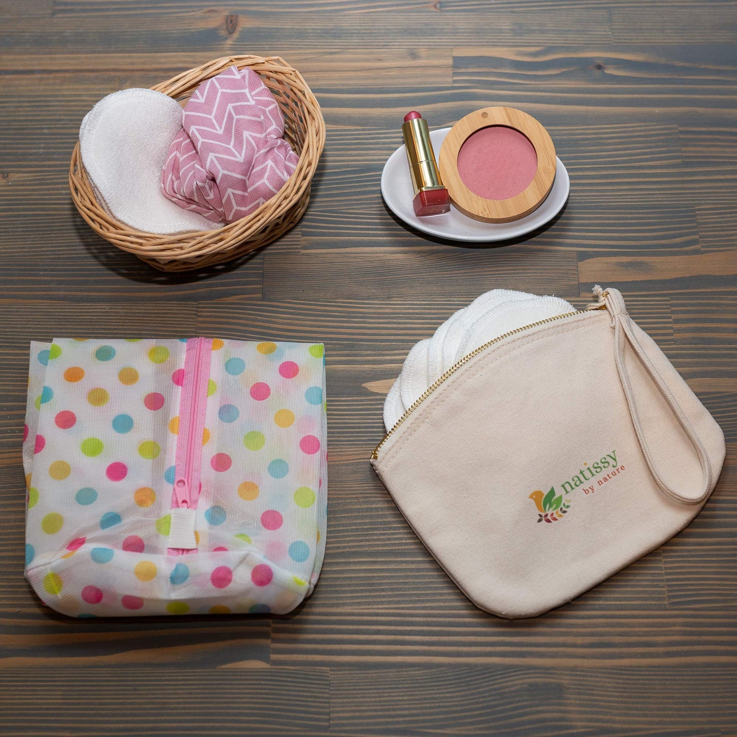A polka-dot bag, cloth pouch, basket with reusable pads, and makeup items on a wooden table