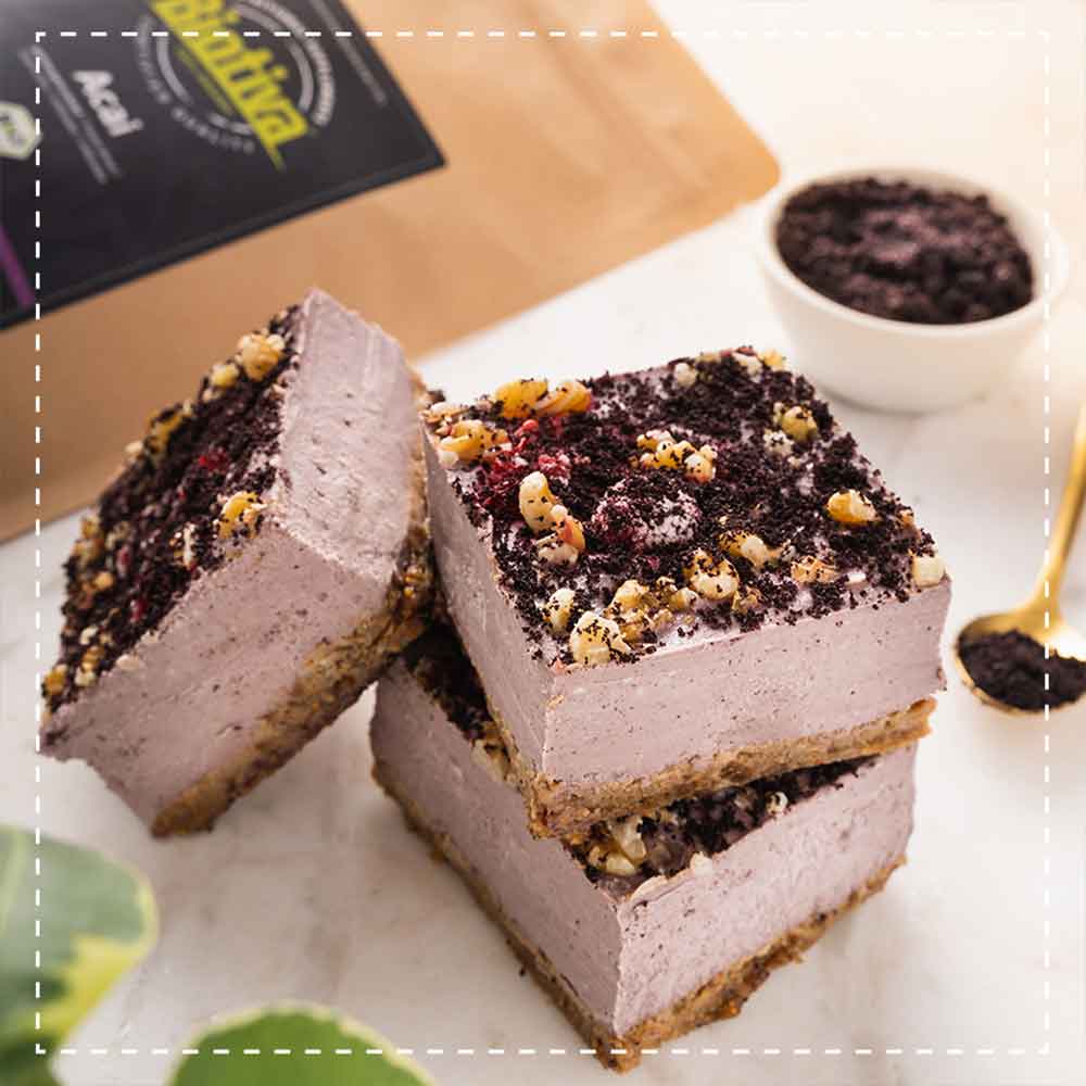 Three creamy blueberry acai dessert bars topped with nuts and powder, stacked on a marble surface