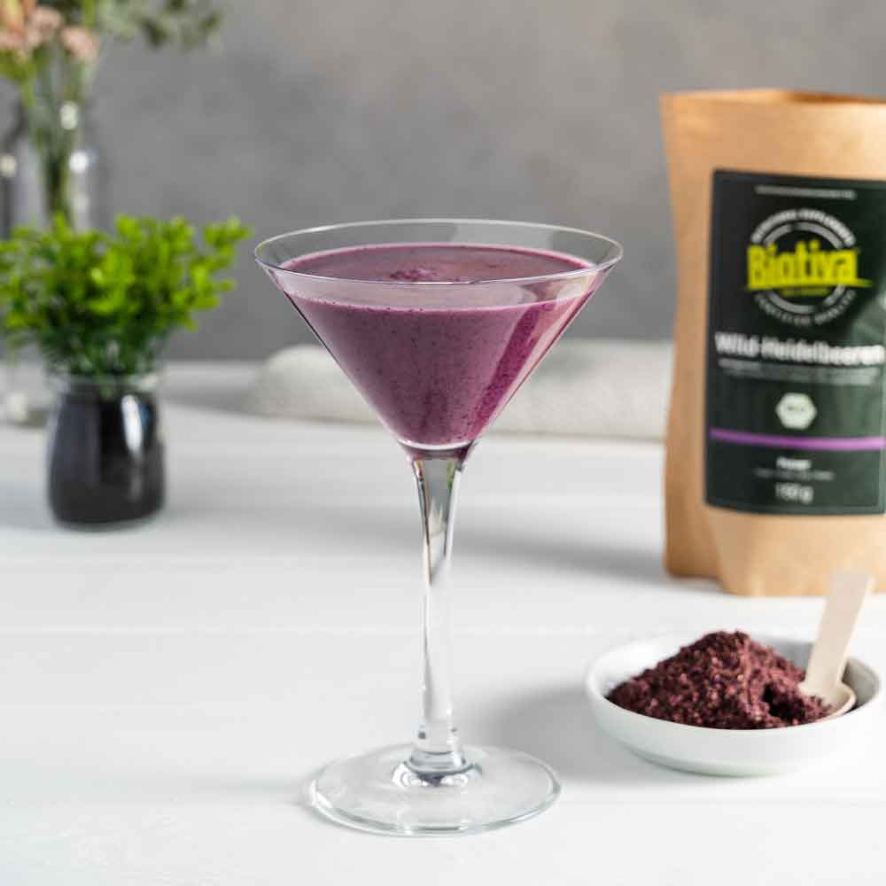 A martini glass filled with wild blueberry smoothie next to Biotiva powder and fresh decor