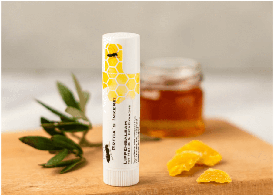 Honey Lip Balm Care Stick shown on a wooden board with honey and leaves.