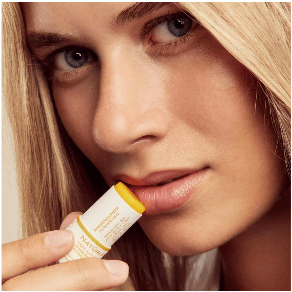 Woman applying Phystine Lip Care No.2, a natural, vegan lip balm with orange and sea buckthorn for nourished lips.