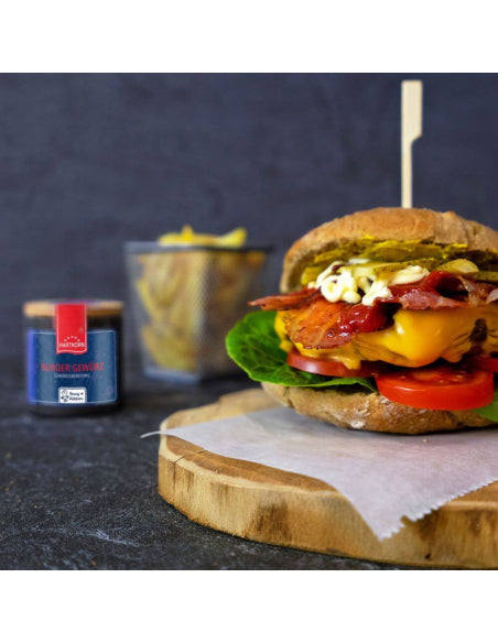 Burger Gewürz jar beside a stacked cheeseburger with fries in the back