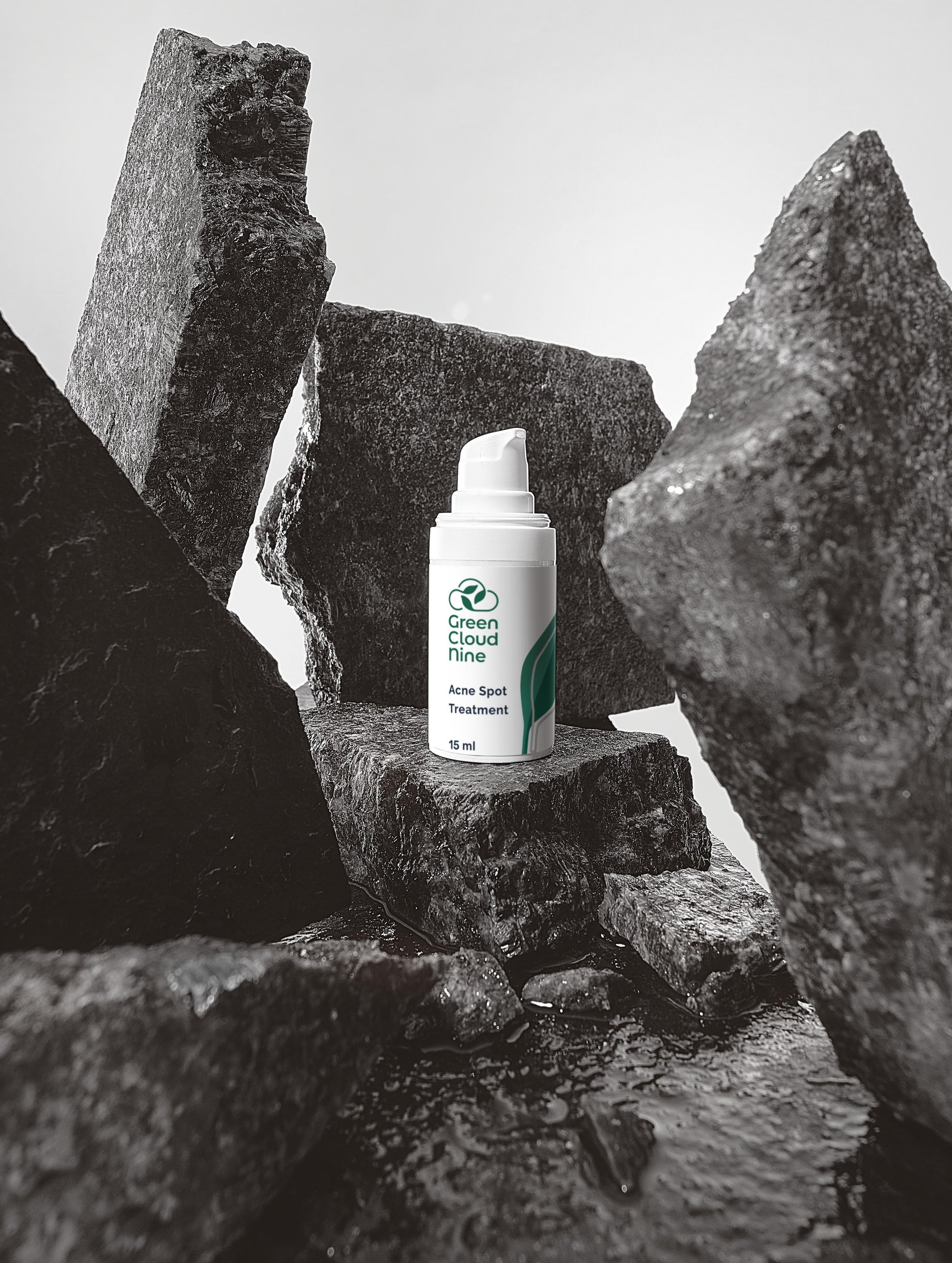 Green Cloud Nine Acne Spot Treatment white pump bottle placed among dark textured rocks