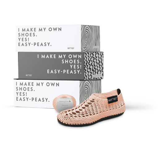 A crocheted peach shoe, spool of thread, and three boxes from BottiesXSchachenmayr
