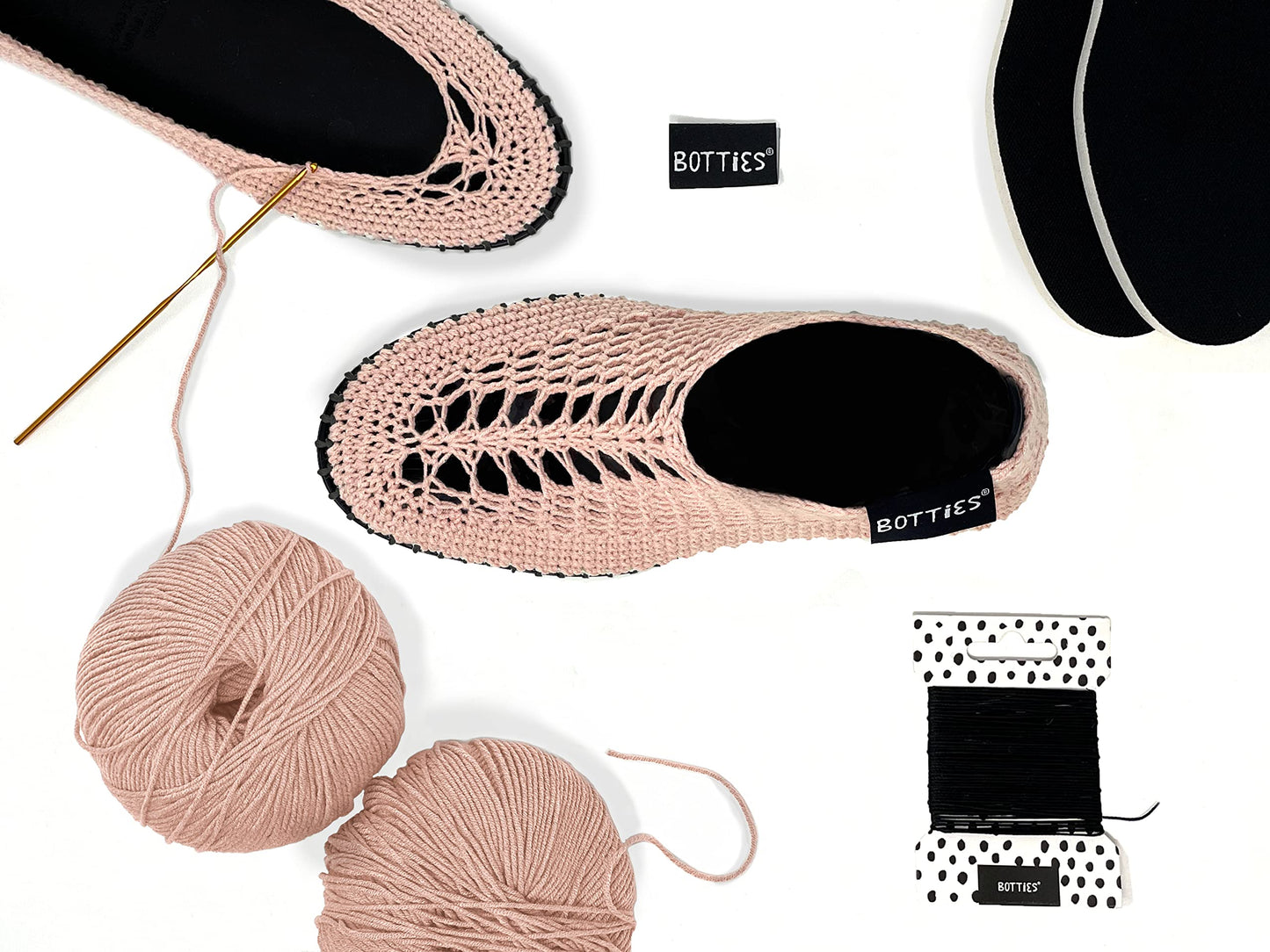Top view of peach crocheted Botties, yarn balls, crochet hook, and black soles ready for crafting.