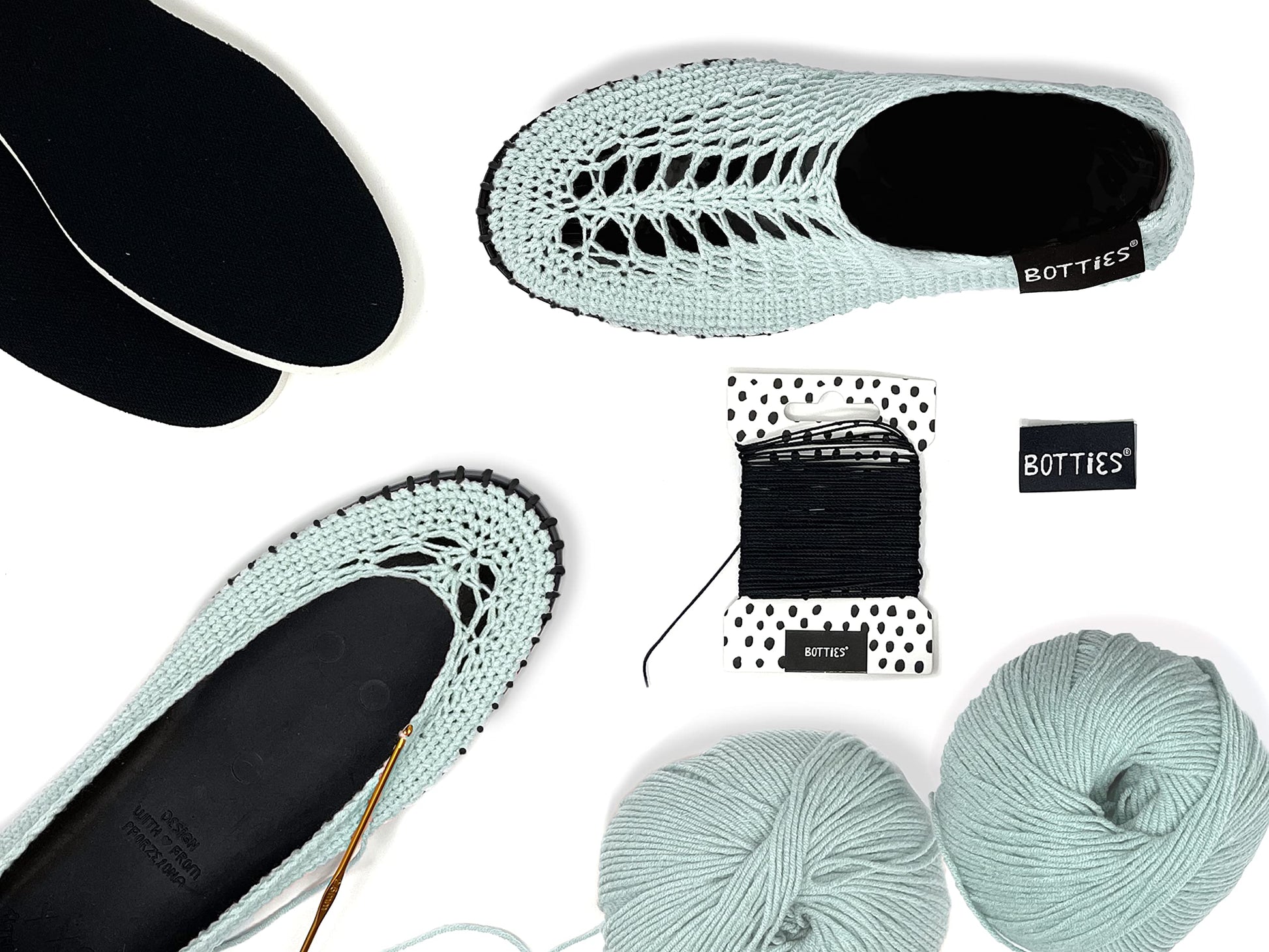 Top view of peppermint crocheted Botties, yarn balls, crochet hook, and black soles ready for crafting.