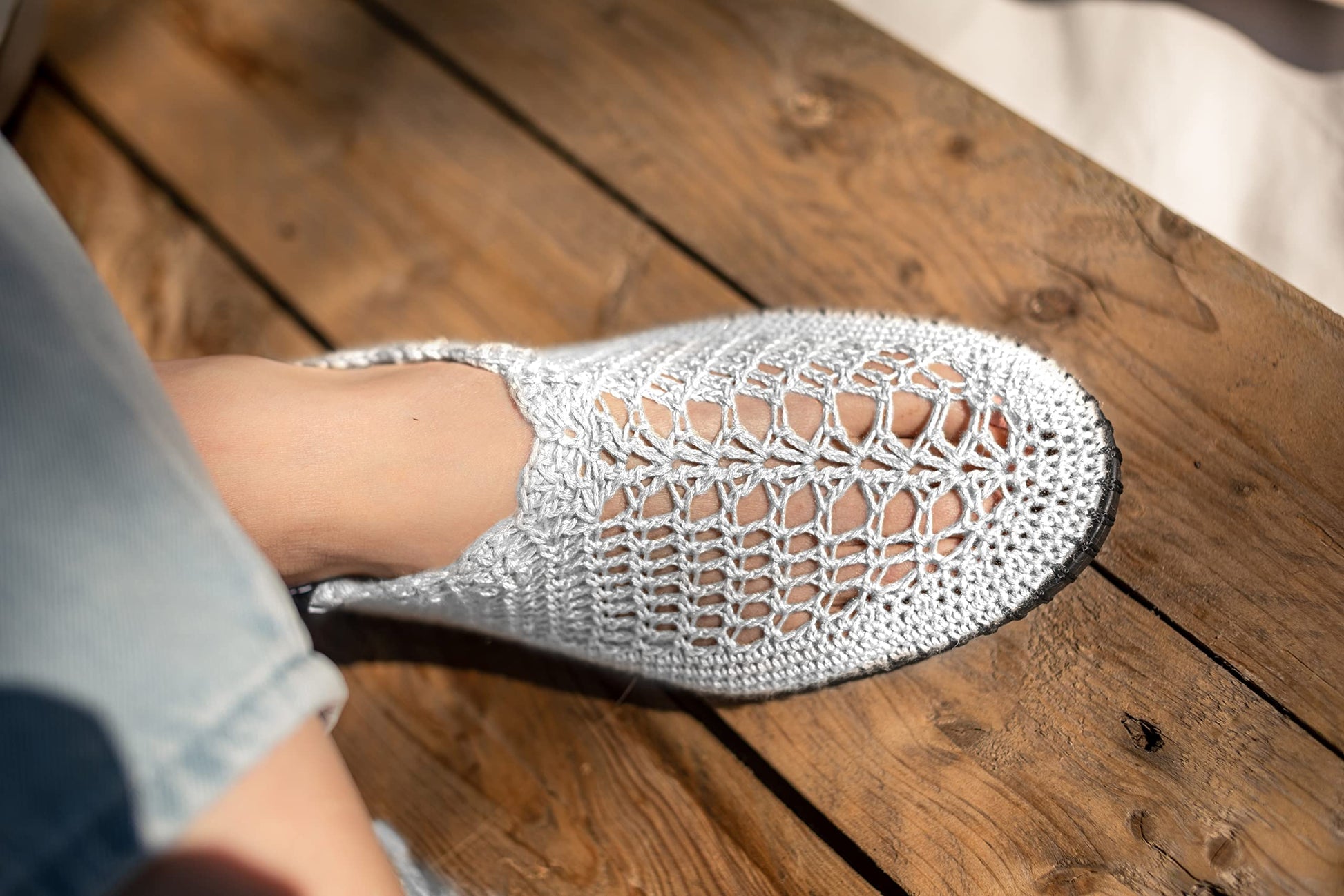 A close-up of a foot wearing a white crocheted Botties shoe on a wooden deck.