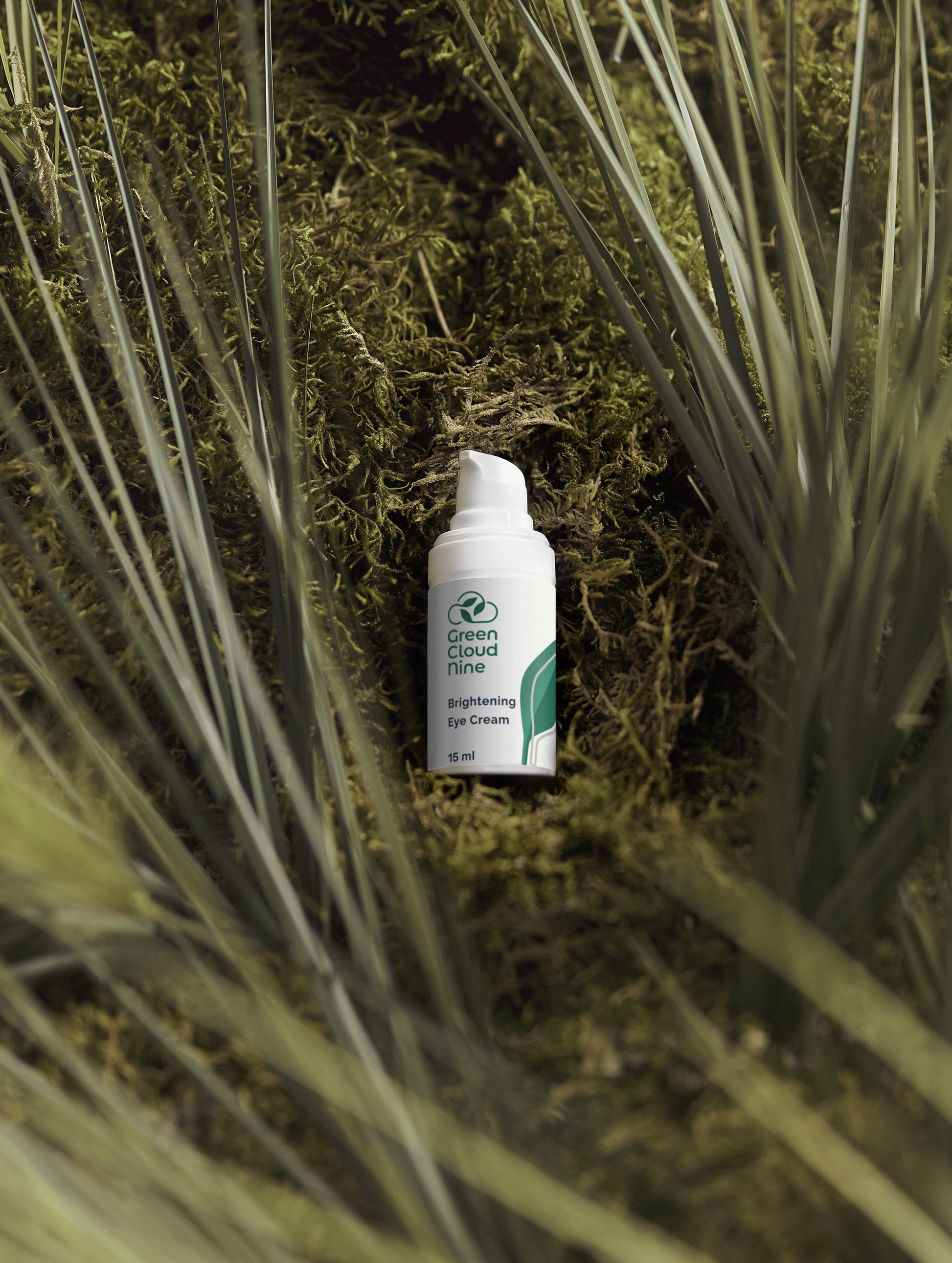 Brightening Eye Cream White bottle pump with Green Cloud Nine label on a bed of green plants (front).