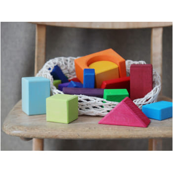 Colorful Grimm’s wooden blocks in various shapes on a wooden chair, ideal for creative play and learning.