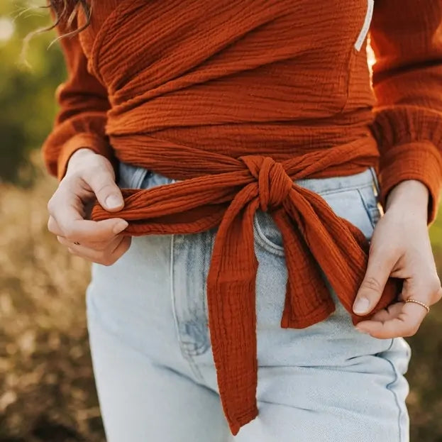 Close-up of Rust-colored muslin wrap blouse with long sleeves and tie waist