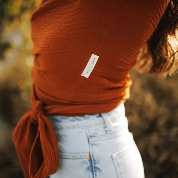 Close-up of Rust-colored muslin wrap blouse with long sleeves and tie waist