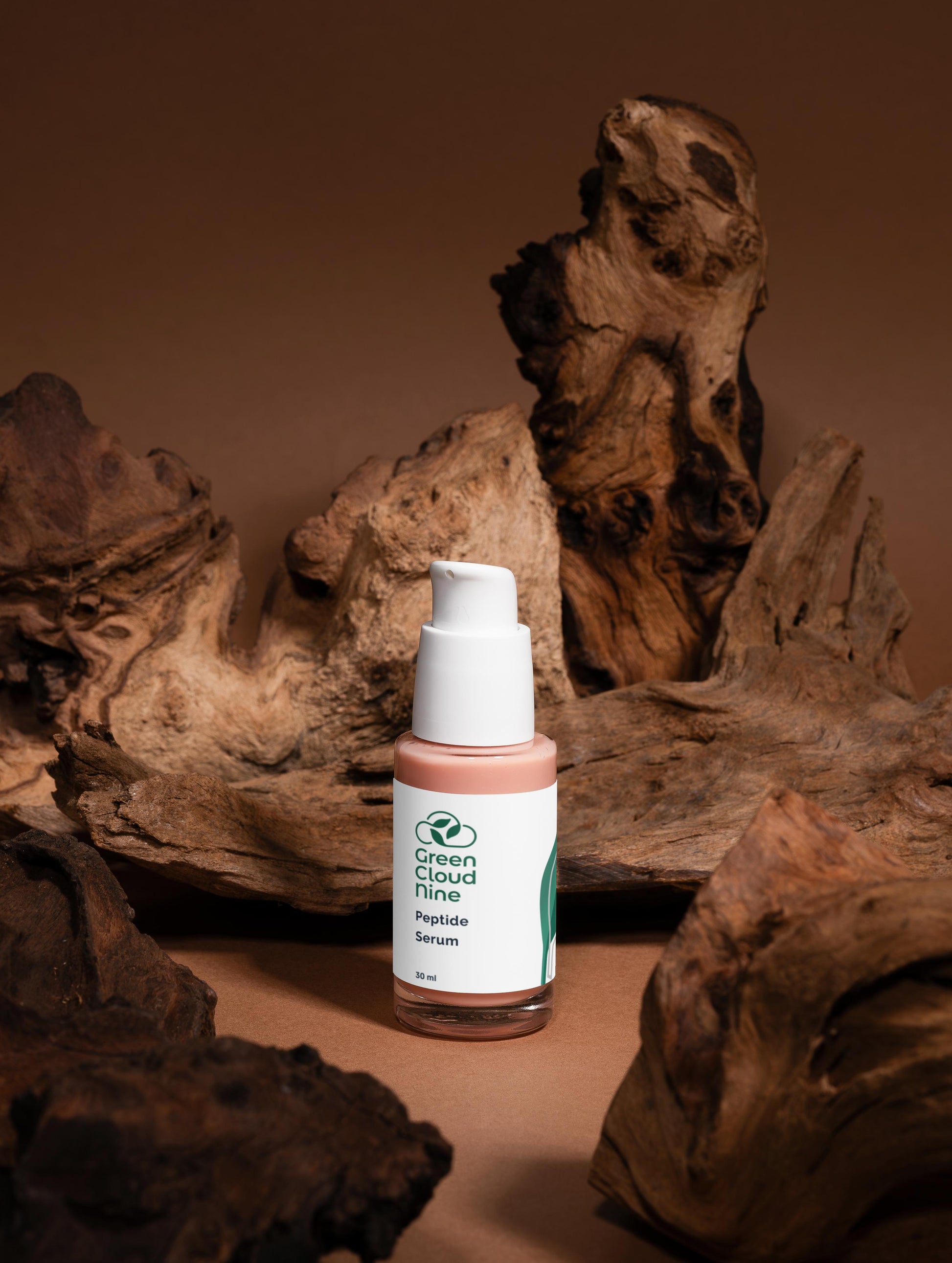 Bottle of Green Cloud Nine Peptide Serum on a brown background with natural wood elements.