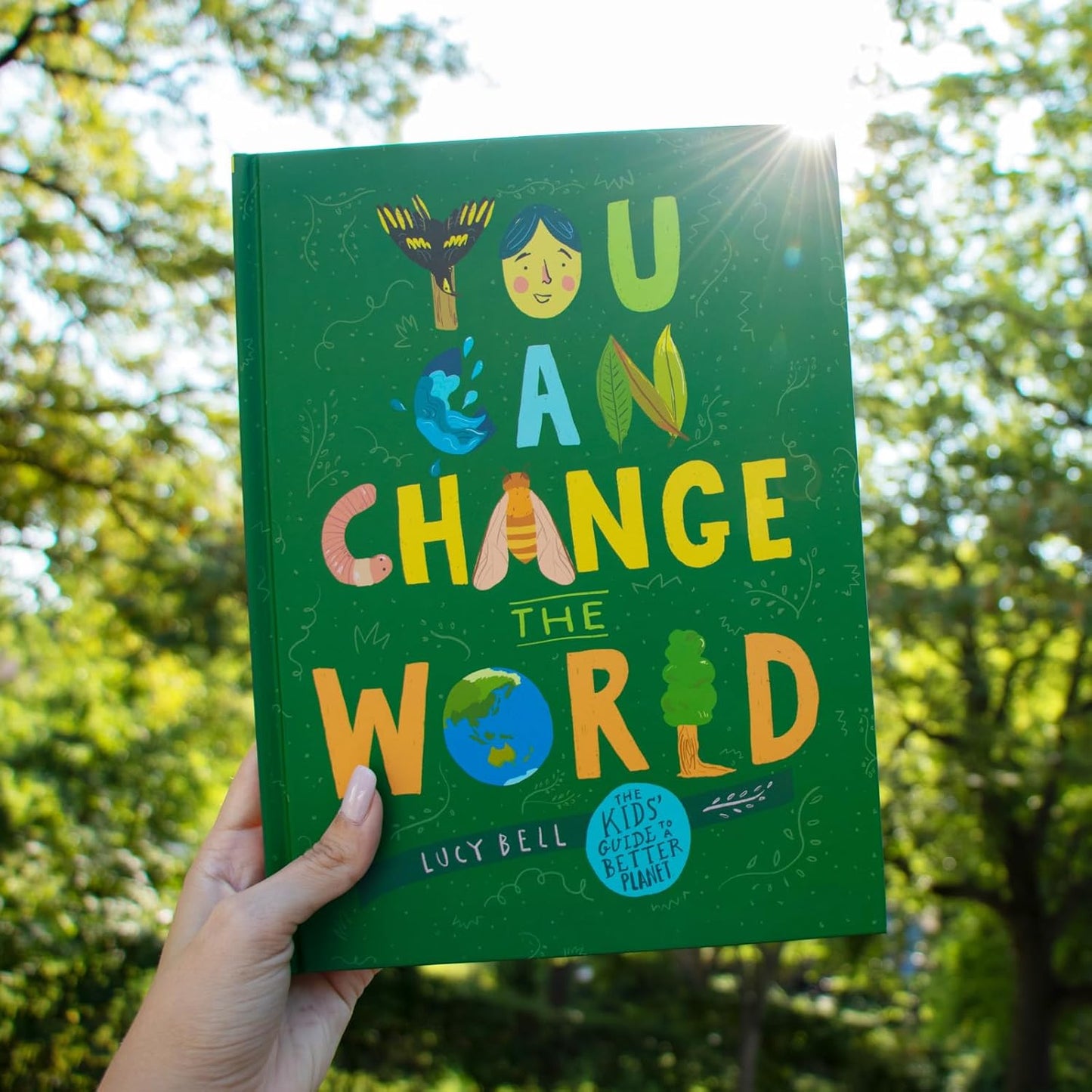 Book titled 'You Can Change the World' held in front of a tree